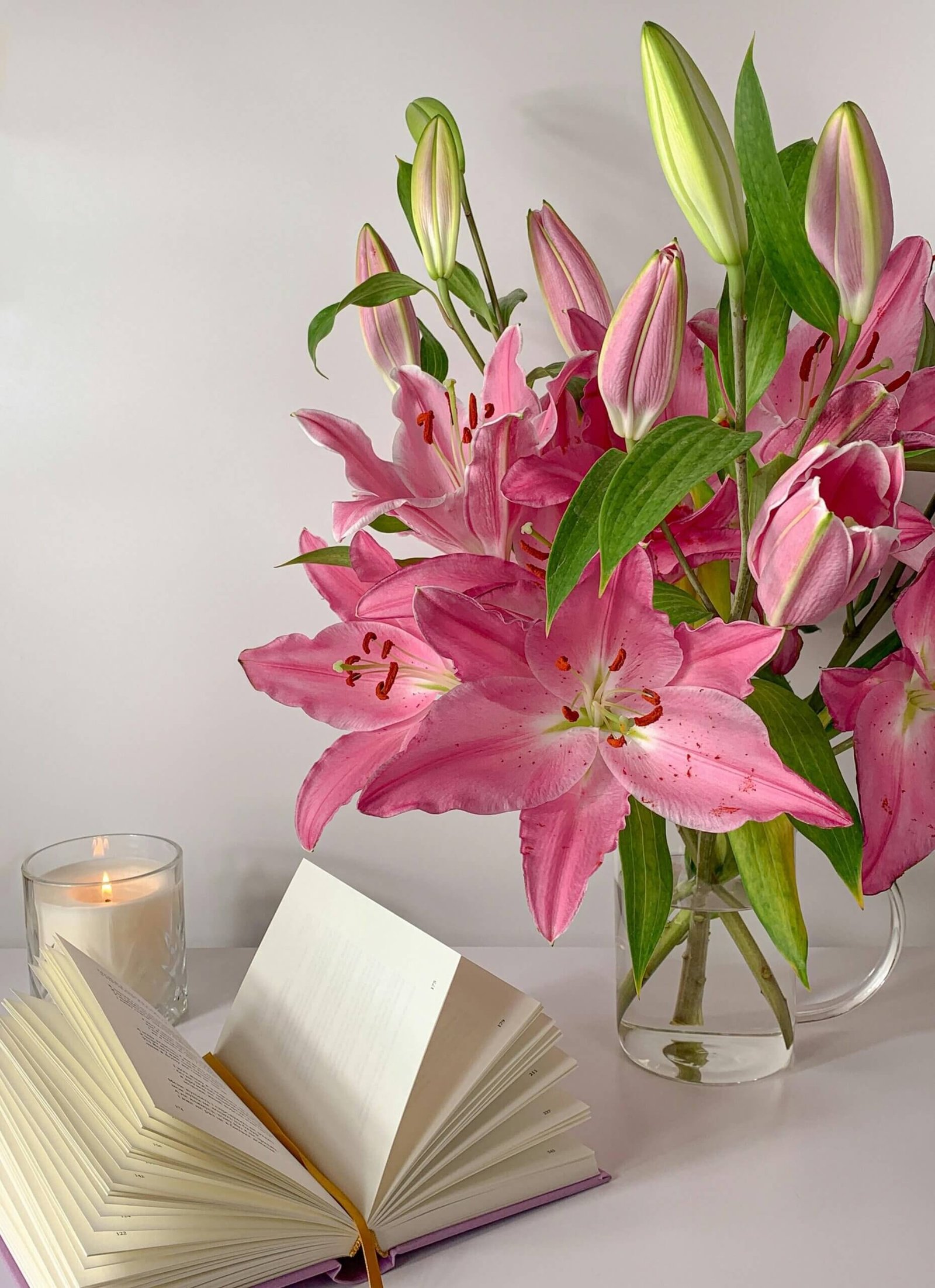 Bougie avec un livre et un lys dans vase.