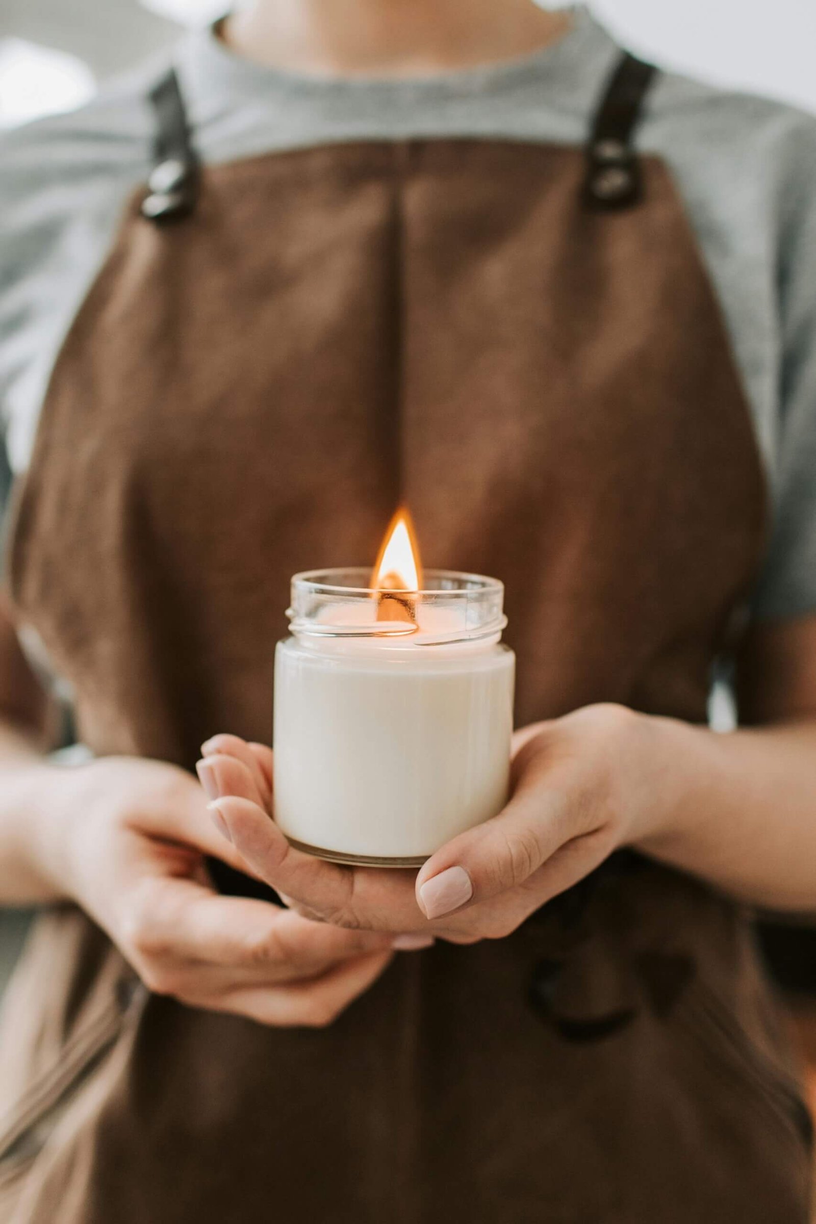 Bougie dans un pot en verre tenue dans les mains d'un artisan avec un tablier.