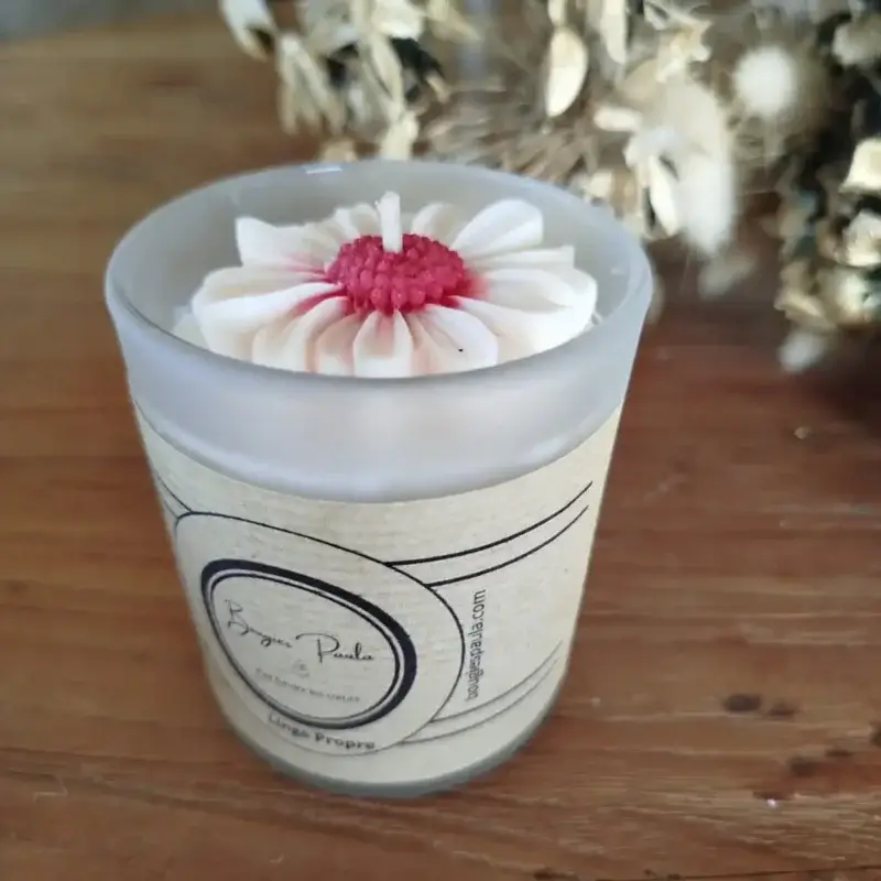 Bougie dans un verre givré transparent sur le quel est posé une marguerite avec le coeur de la fleur rouge et les pétales blanches.
