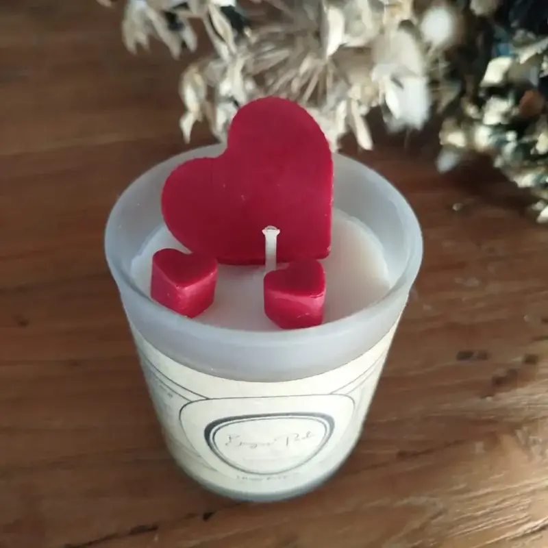 Bougie dans un verrre givré transparent accueillant trois coeurs rouges, symbolisant l'amour en cette Saint Valentin.