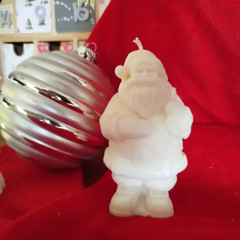 Bougie en forme de Père Noël placé à côté d'une boule argentée avec un fond en décor rouge.